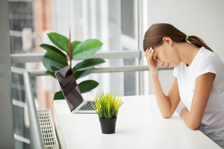 Thrive Mind & Wellness Center | Young woman working at office desk in front of laptop suffering from chronic daily headaches