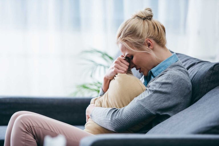 Thrive Mind & Wellness Center | A woman with post-partum sadly hugs a pillow.